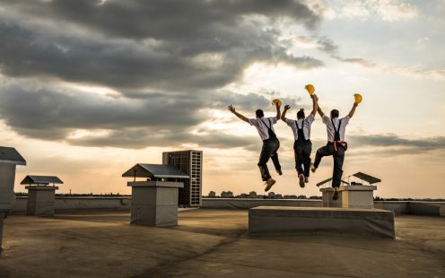 Rear view of construction workers jumping with raised arms on a roof and celebrating because they managed to complete the construction of the building. Copy space.