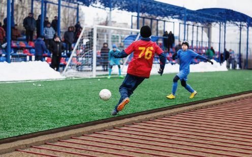 Young Active sport heathy boys in red and blue sportswear running and kicking a red ball on football field with artificial turf. soccer youth team plays football. activities for kids, training