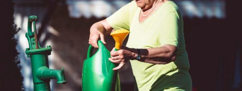 Senior woman in her garden outdoors preparing to water the plants, caring, love the nature, backyard