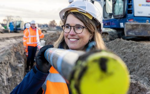 Two smiling people carry a black and blue water supply pipe.